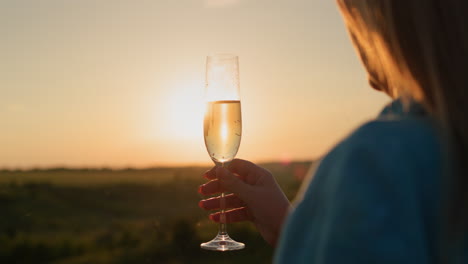 successful woman with a glass of champagne on the background of a picturesque valley at sunset