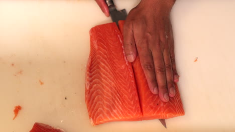 chef cortando el filete de carne de salmón por la mitad y separándolo de su piel para un plato de sushi