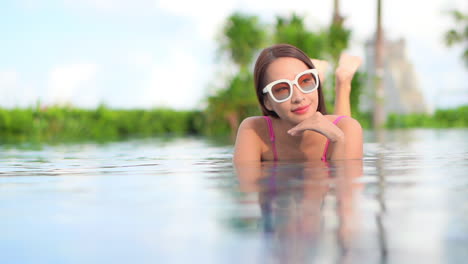 Eine-Hübsche-Junge-Frau,-Die-In-Einem-Resort-Schwimmbad-Auf-Dem-Bauch-Liegt,-Lächelt,-Als-Sie-Sich-In-Der-Landschaft-Umsieht