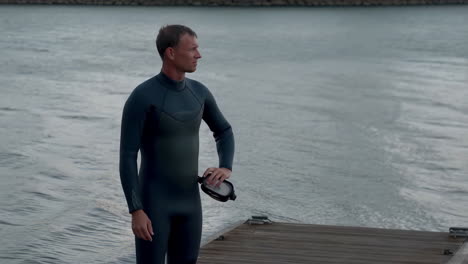 man in wetsuit on a dock with diving mask