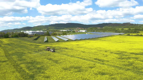 tractor spraying pesticide around solar panels in a rapeseed field