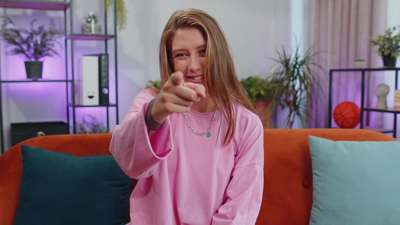 Jovem mulher sorridente apontando para a câmera, escolhendo um vencedor, indicando, convidando e aprovando em casa.