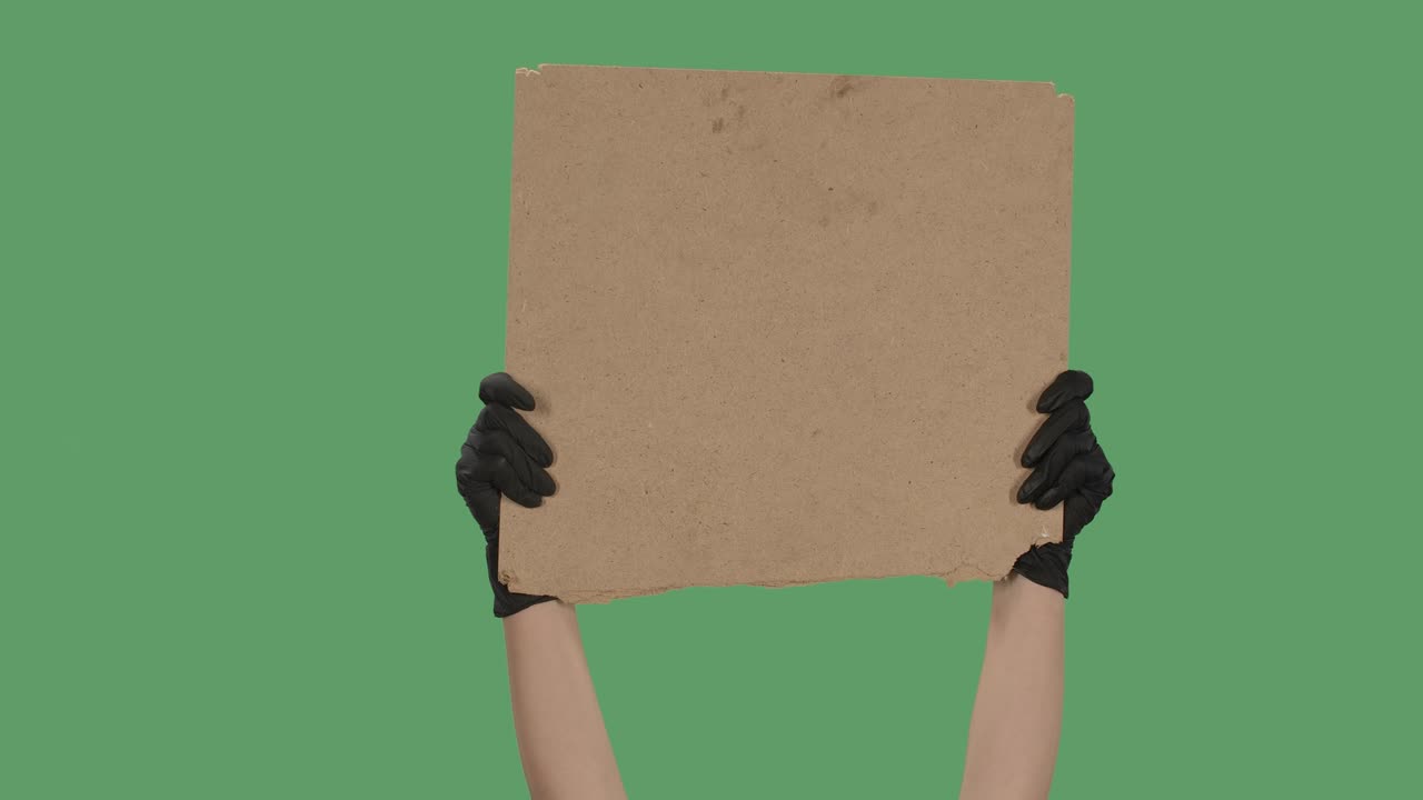 검은 장갑을 입은 손은 카드보드 상자에서 빈 포스터를 들고 슬로건, 로고 또는 광고를위한 빈 공간, 배너 디자인 개념, 녹색 화면, 크로마 키, 클로즈업, 느린 모션.
