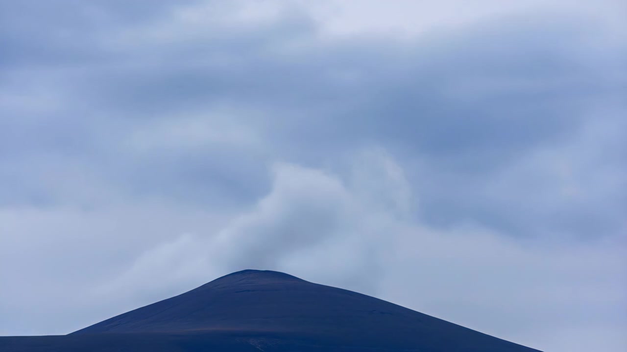 淡い曇り空の下、シーンの下部には濃い青色の丸みを帯びた丘が広がり、中央には低い頂がある。広々としたネガティブスペースが、柔らかく落ち着いたトーンで穏やかなミニマリストの風景を作り出している。