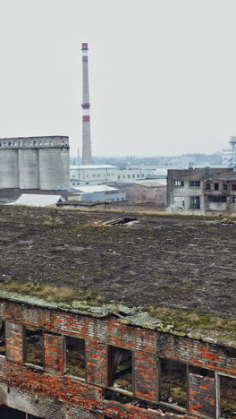 an old abandoned factory hangar with damaged walls on the background of other old structures in the same area. aerial view. vertical video