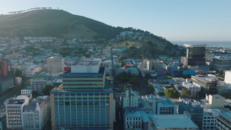 Fliegen-Sie-über-Der-Stadt,-Die-Von-Heller-Sonne-Beleuchtet-Wird.-Schöner-Tag-Mit-Klarem-Himmel.-Verschiedene-Gebäude-Und-Wohnviertel-In-Hanglage.-Kapstadt,-Süd-Afrika