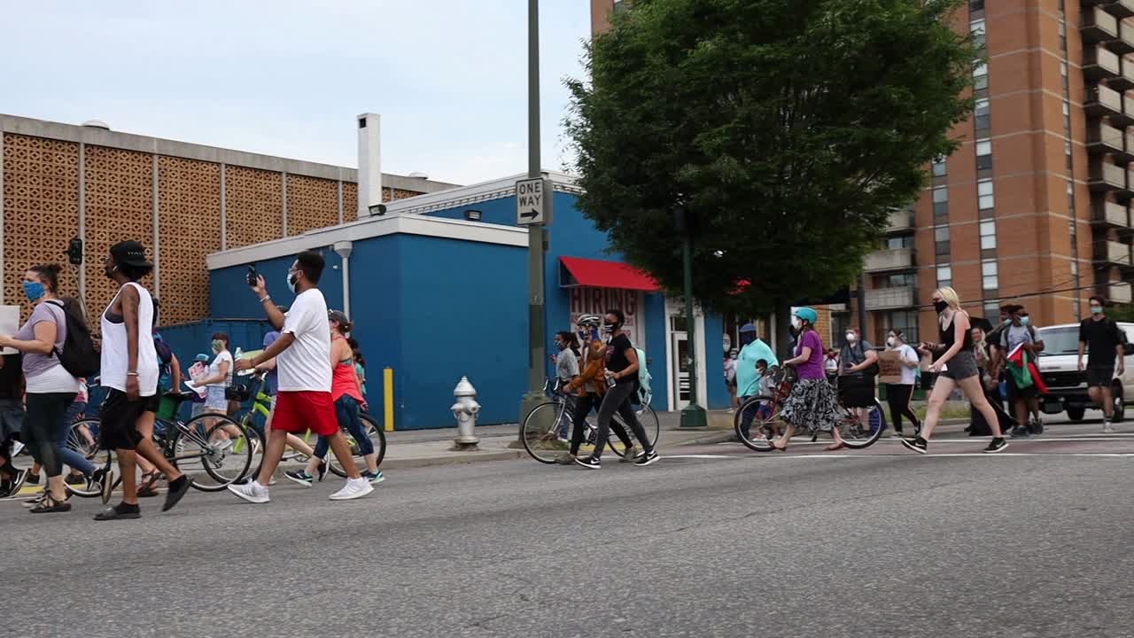 Demonstrators march through the streets carrying signs, chanting and wearing masks due to coronavirus concerns as they protest racial discrimination and police violence. Slow motion.