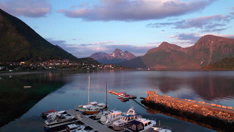 aerial dolly forward shot of boats in a small marina in a bay with a village on the slopes of a mountain on a warm summer evening with mountains and clouds