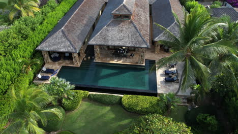 drone shot of luxury private villa with swimming pool, palm trees and green landscape on exotic travel destination