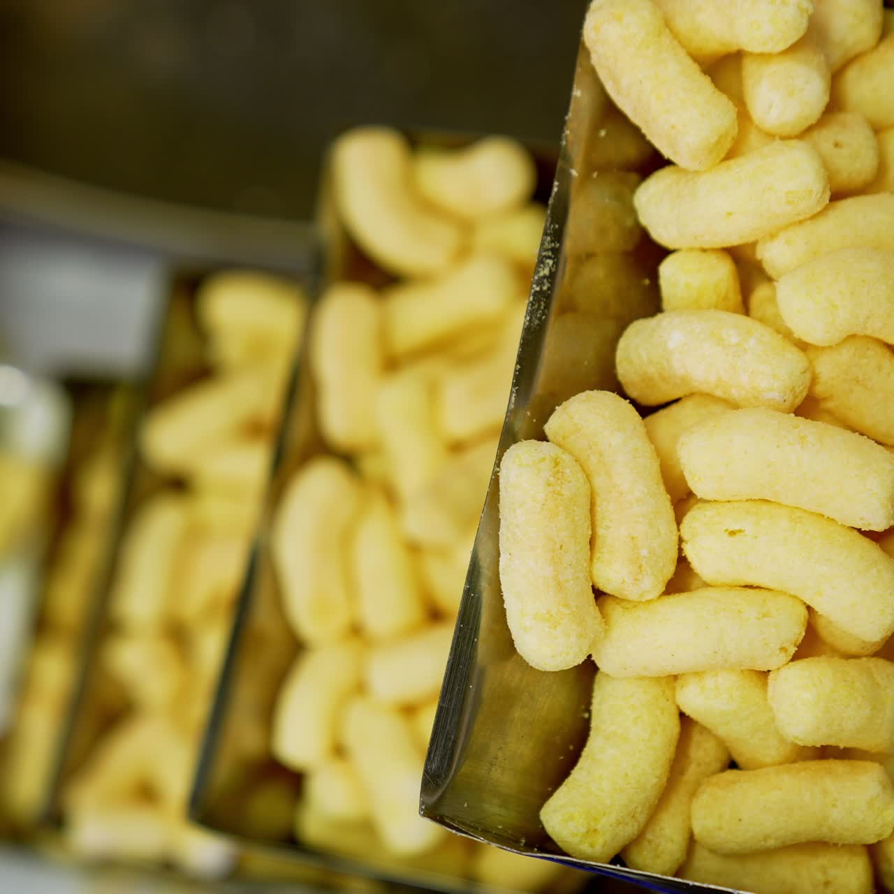 Production process of corn snacks at up-to-date food factory. Crunchy yellow sticks lifted by conveyor belt. Close up