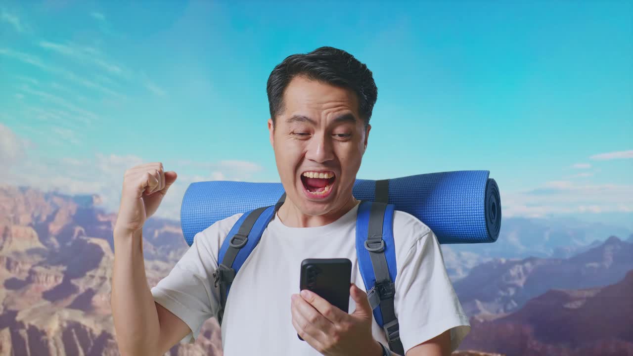 Close Up Of Asian Male Hiker With Mountaineering Backpack Looking At The Smartphone And Screaming Goal Celebrating The Success While Traveling At The Top Of Mountain