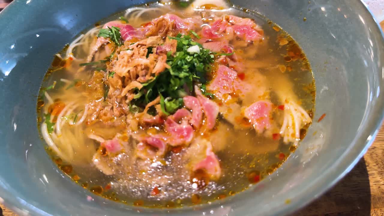 A steaming bowl of beef pho with fresh herbs and noodles, captured in a vibrant Bangkok restaurant setting