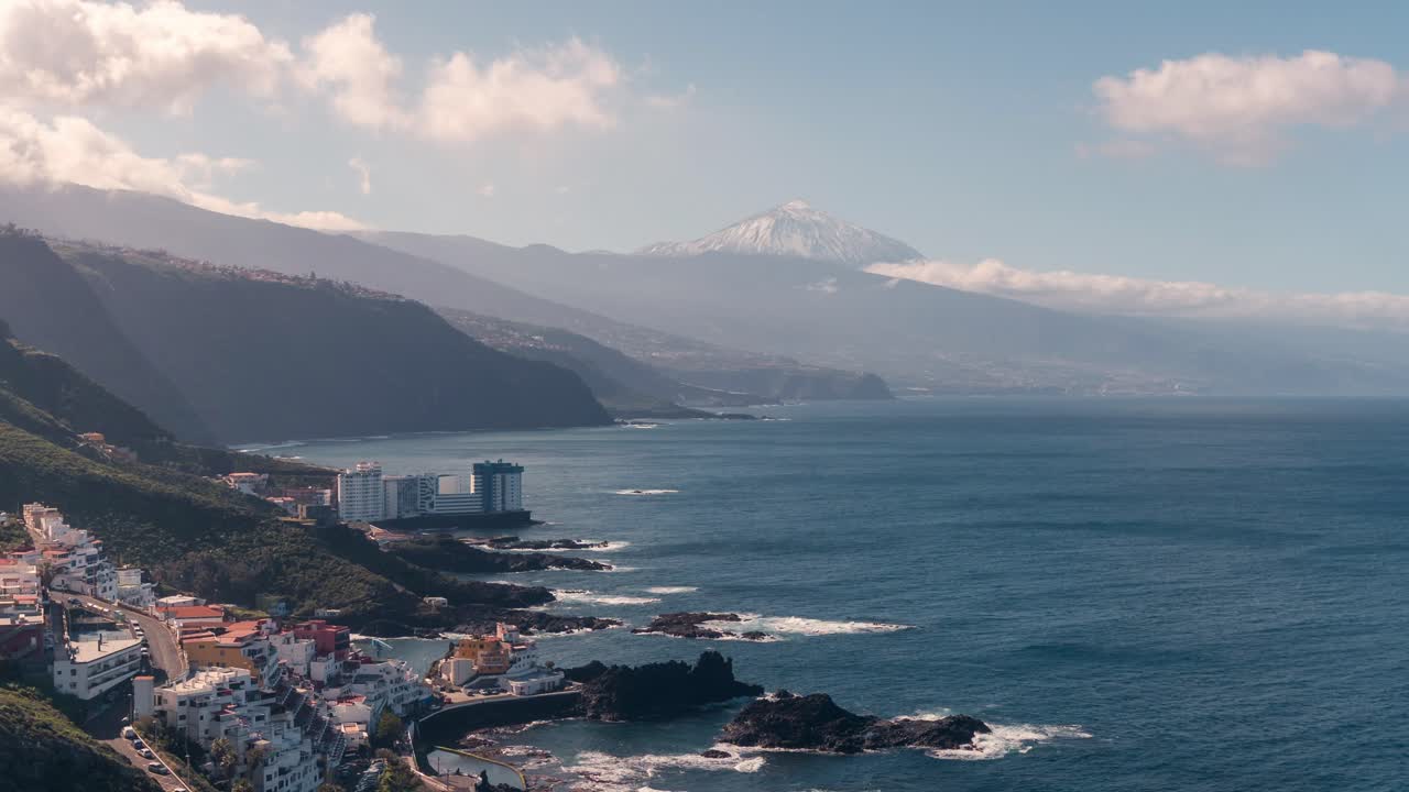 Vista timelapse diurna del vulcano Teide e della costa settentrionale di Tenerife, Isole Canarie. Il Teide innevato che si erge sull'Oceano Atlantico, aspre scogliere costiere, villaggi
