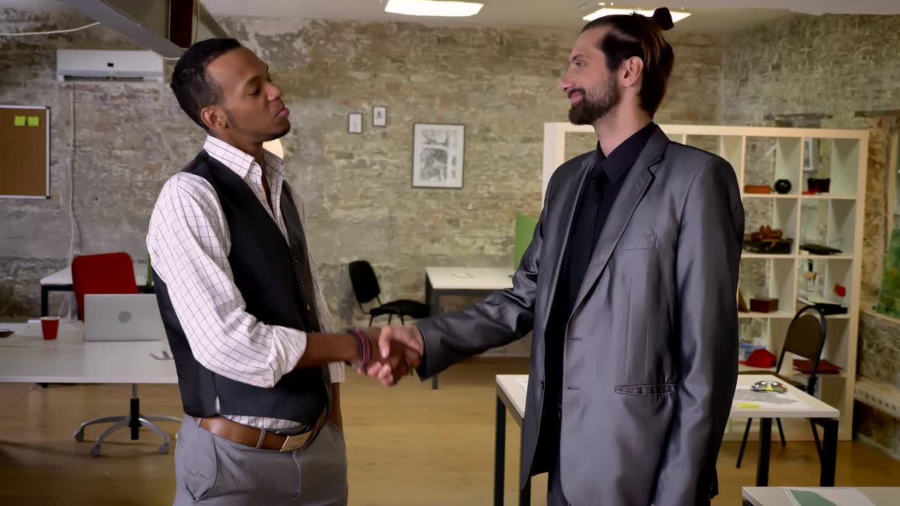 Due lavoratori multietnici si stringono la mano in ufficio, concetto di comunicazione