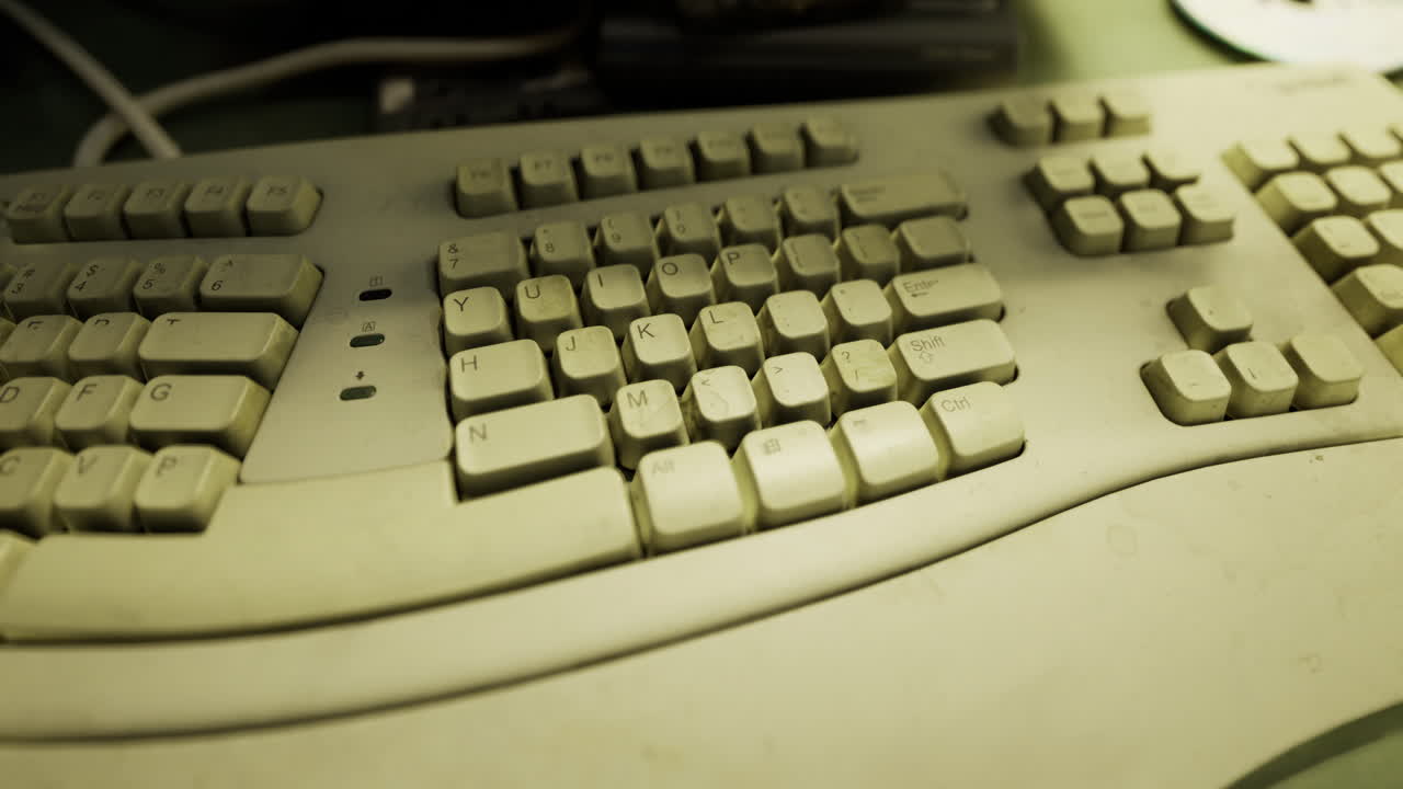 Old dusty keyboard resting on a cluttered desk filled with tech gadgets