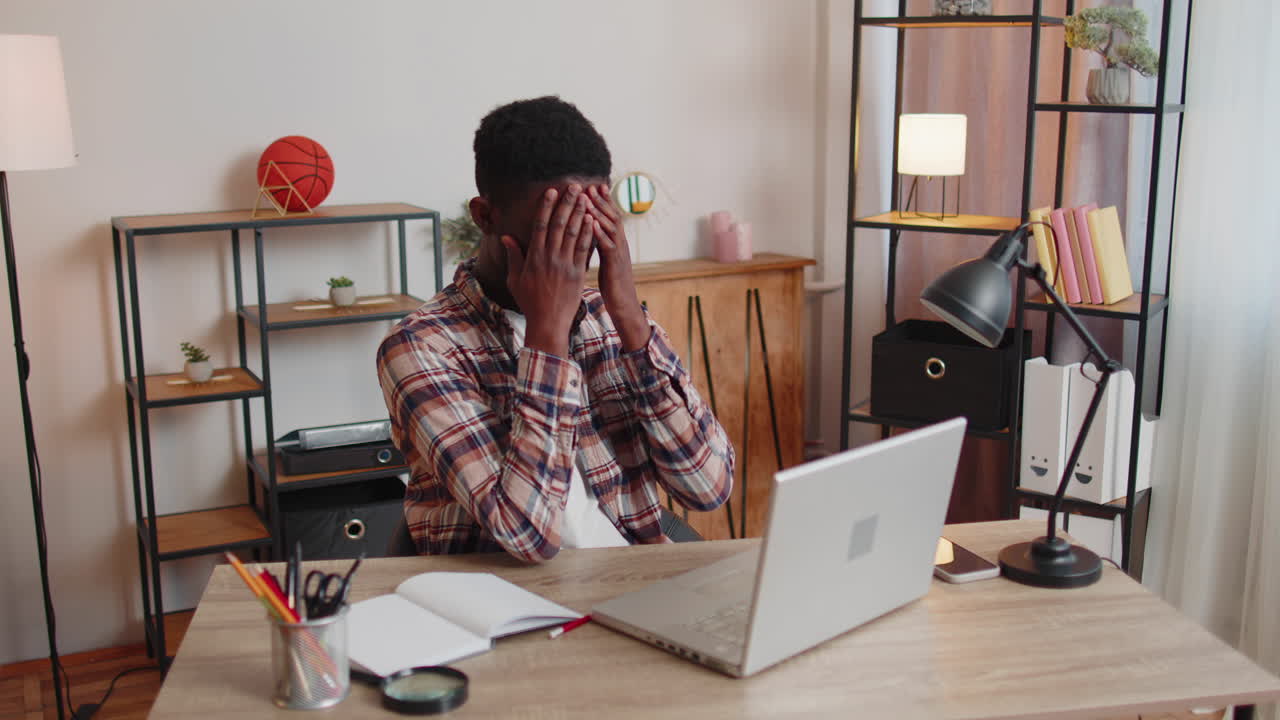 Tired man teacher using laptop computer suffering from tension, migaine headache at home office