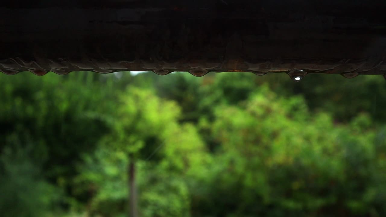 drops of water fall from the metal surface of a pipe during a summer rain