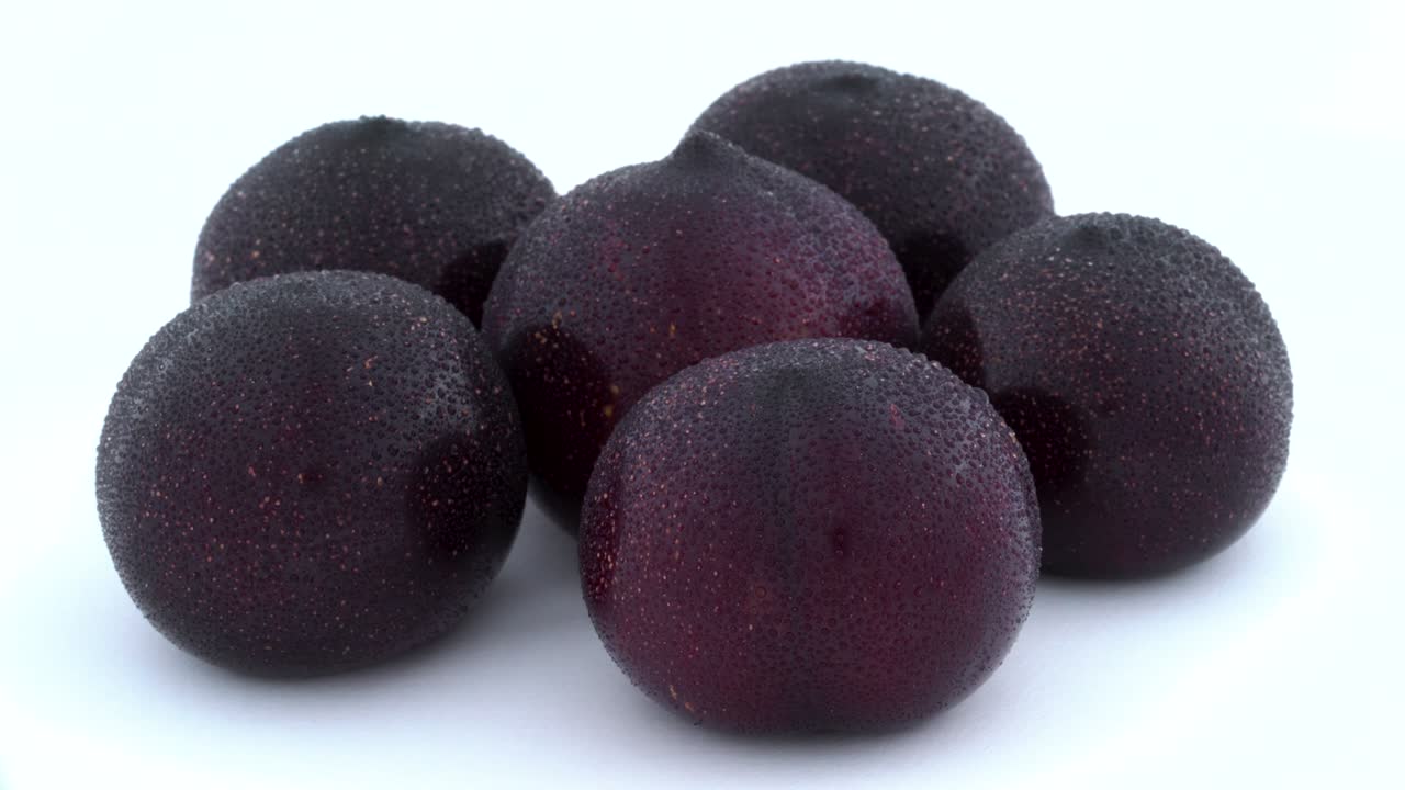 несколько больших фиолетовых слив с каплями воды. вращающиеся на поворотном столе. изолированные на белом фоне. крупный план. макро.