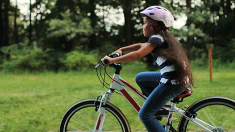 retrato de una niña con casco de bicicleta ciclando bajo algunos árboles en un parque. cámara en movimiento. fondo borroso