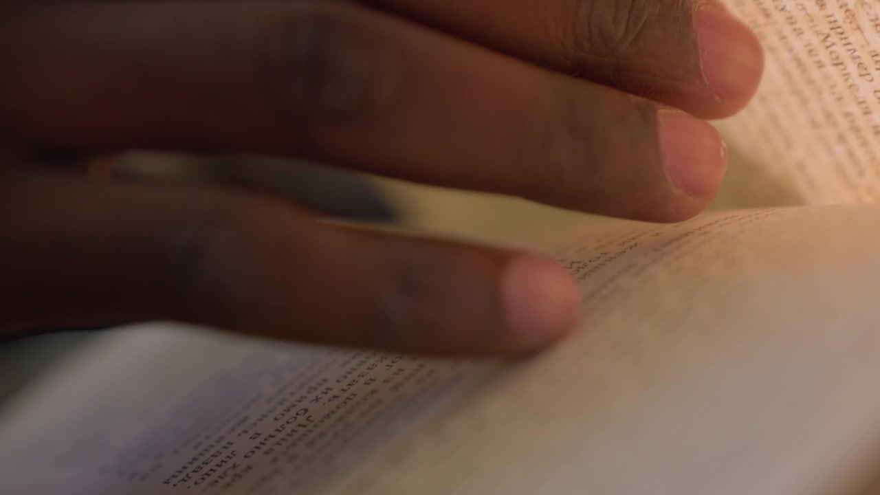 Close up of hand turning pages of open book with text visible. fingers move steadily across multiple sheets revealing printed words and lines in soft natural light. Background remains out