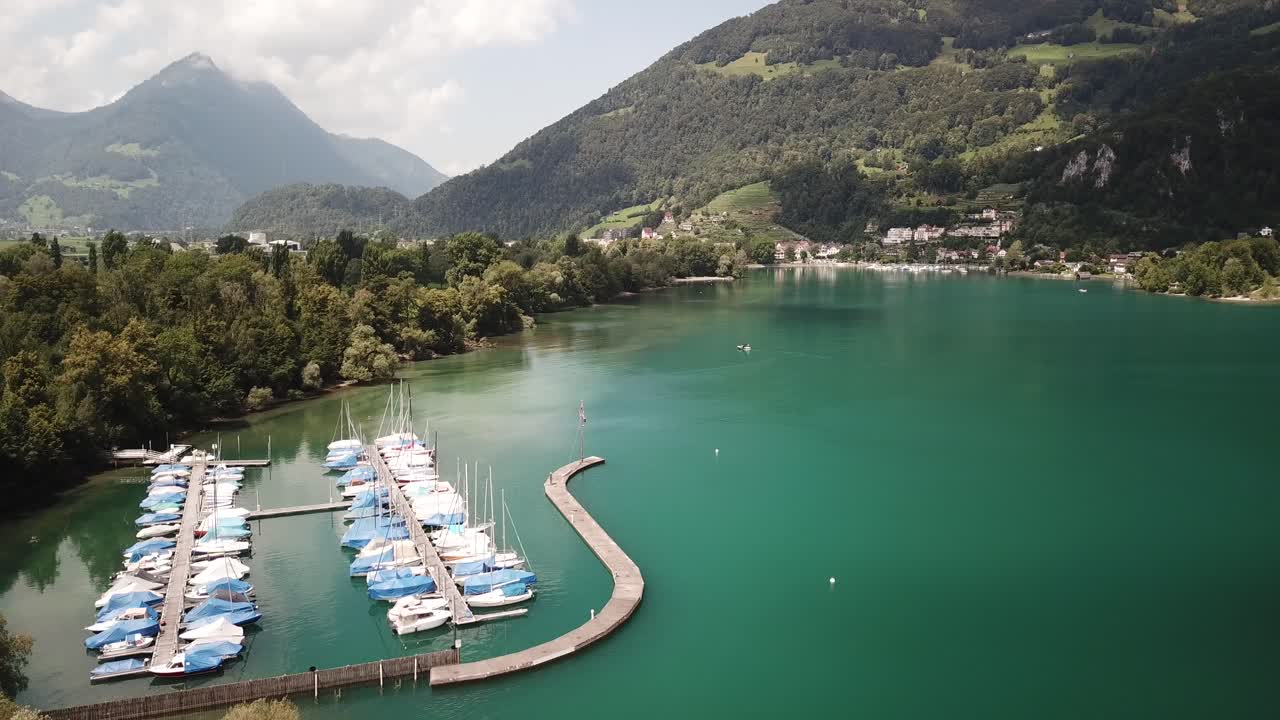 Small boats moored at a wooden scaffolding in a turquoise lake between the high mountains of the Alps in Switserland on a bright day.