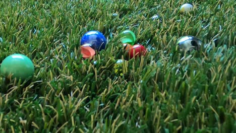 close up of a game of marbles that hit each other in slow motion, bouncing and spinning on grass