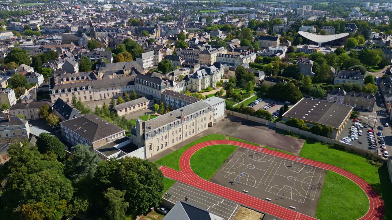 Drone slowly pulling out over the historic Lycée Douanier Rousseau complex in Laval, Mayenne, France, revealing heritage buildings, modern sports track, and the northern cityscape