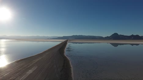 Eine-Drohnenaufnahme,-Die-über-Die-Bonneville-Salinen-Fliegt,-Zeigt-Den-Damm-Der-Salinen,-Der-Die-überflutete-Salzpfanne-Teilt