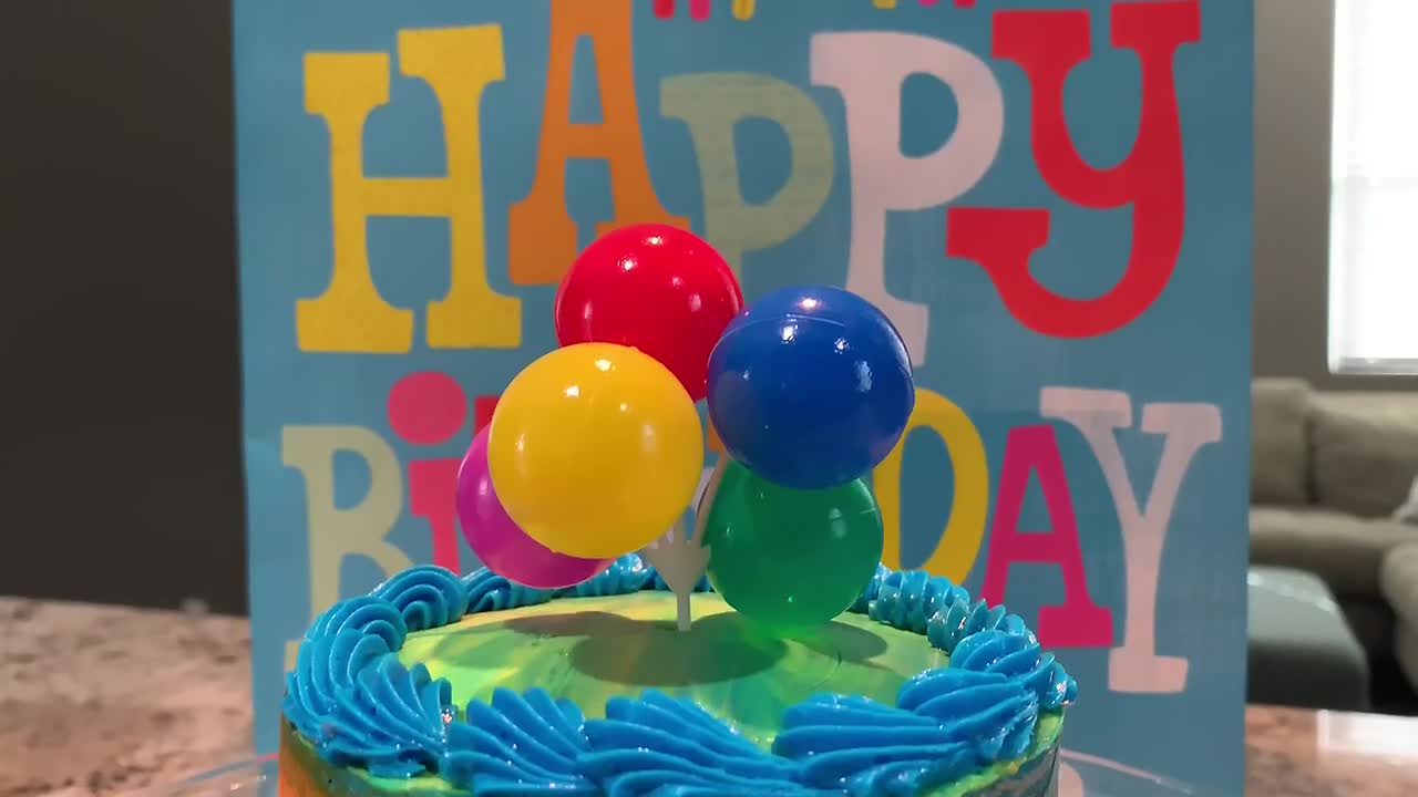 un pastel de cumpleaños colorido en un soporte de pastel de vidrio con un lindo ramo de globos como adorno para el pastel