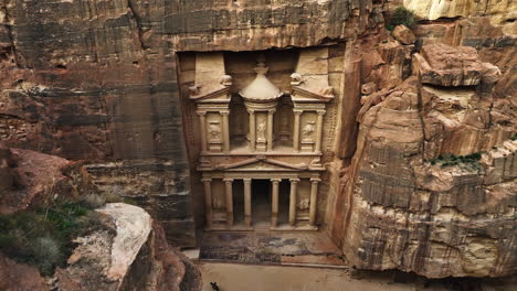 Aerial-view-over-cliffs,-tilting-toward-the-Treasury,-Al-Khazneh-in-Petra,-Jordan