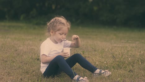 Una-Chica-Bonita-Almuerza-Con-Yogur-En-El-Césped-Del-Parque-A-Cámara-Lenta