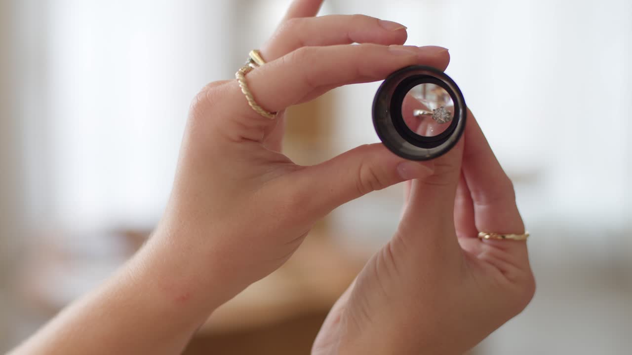 A diamond wedding ring getting looked at through a monocle with a woman's hands and nice bokeh background