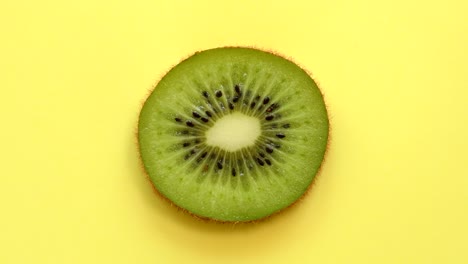 una rebanada de kiwi girando desde arriba sobre un fondo amarillo