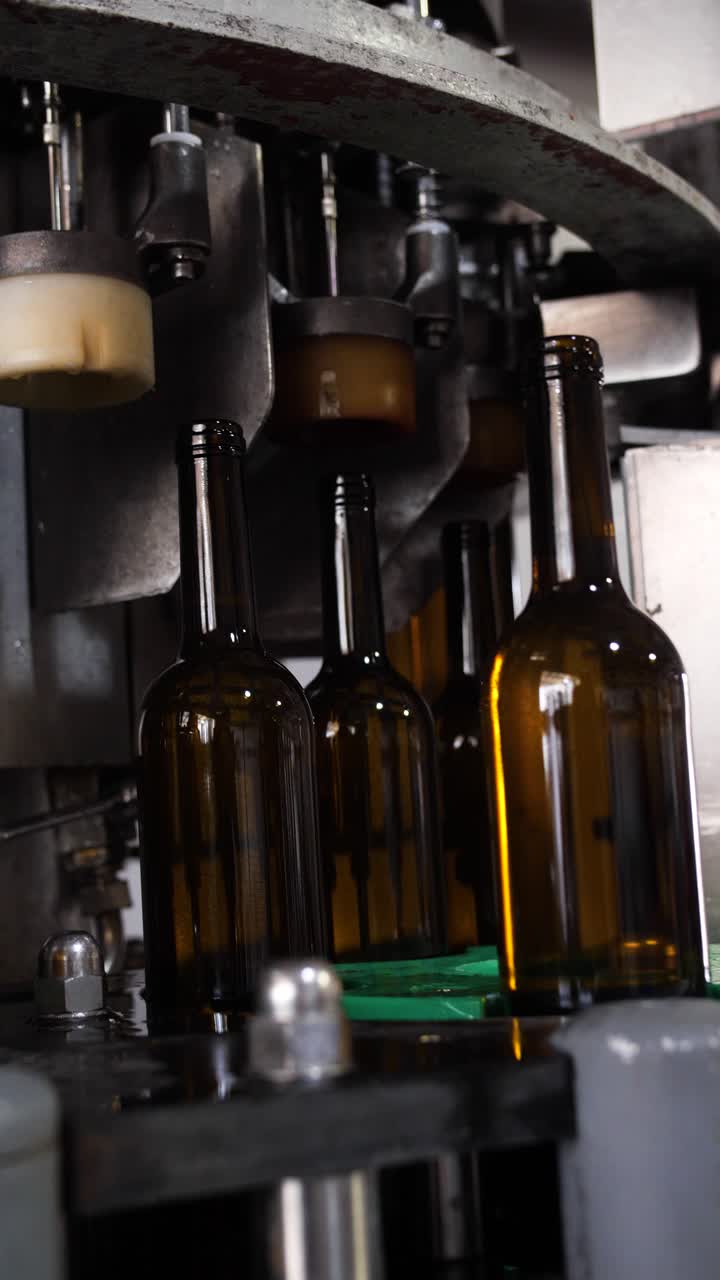 Slow motion close up vertical shot of glass wine bottles been produced in a line on an automatic industrial machinery