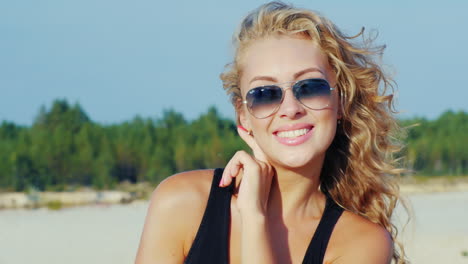 mujer joven con gafas de sol sonriendo a la cámara el viento jugando con su cabello