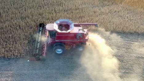 aerial pan view of red combine harvesting beans in farmers field near sundown in the midwest usa