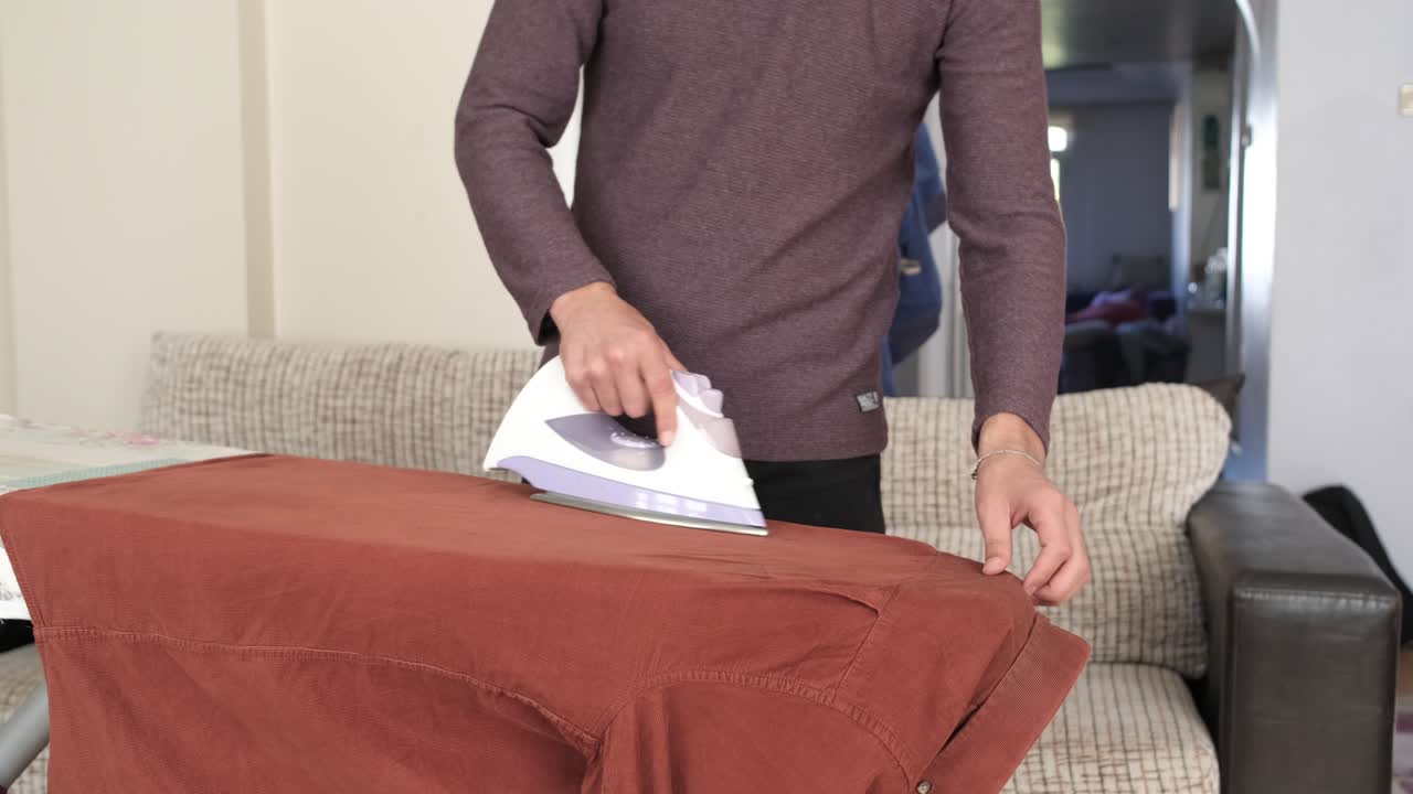 Man ironing the orange shirt on the ironing board at home, people iron before getting dressed, shirt wrinkled