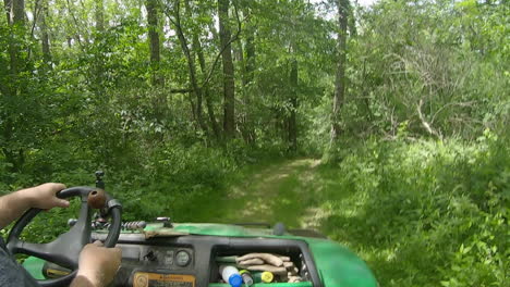 view of hands and steering wheel of a man driving a utv pm a grassy trail through the woods