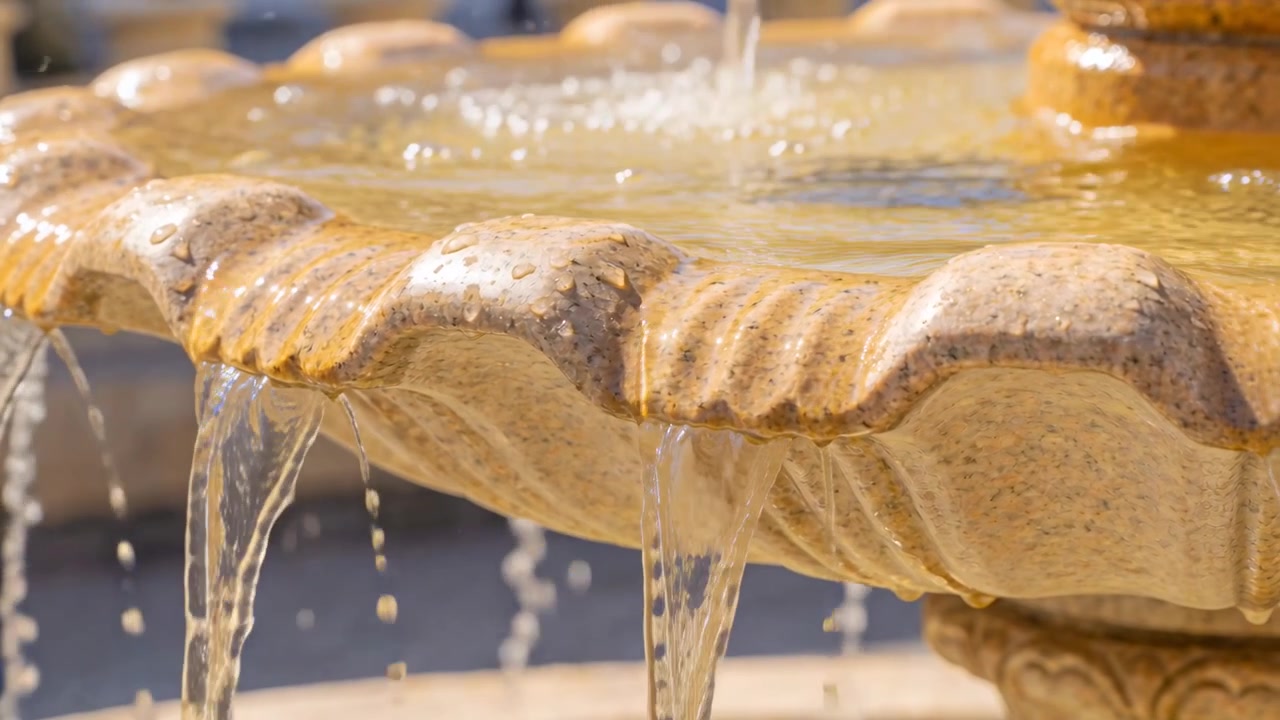 Zampillo centrale che alimenta una fontana a più livelli, traboccando dal bordo smerlato in un cortile, con acqua che circola.