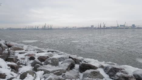 snowy-rocky-shore-in-winter-with-snow-and-ice,-calm-waves,-and-moody-cloudy-sky