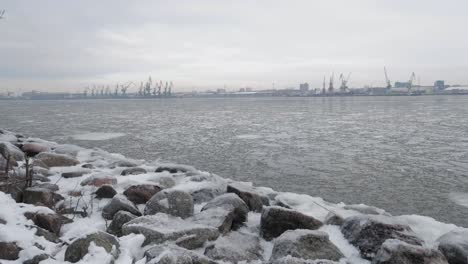 snowy rocky shore in winter with snow and ice, calm waves, and moody cloudy sky