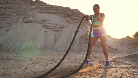 female athlete training outdoors around the sand hills at sunset. active physical activity workout. crossfit. the girl has a rope on the ground