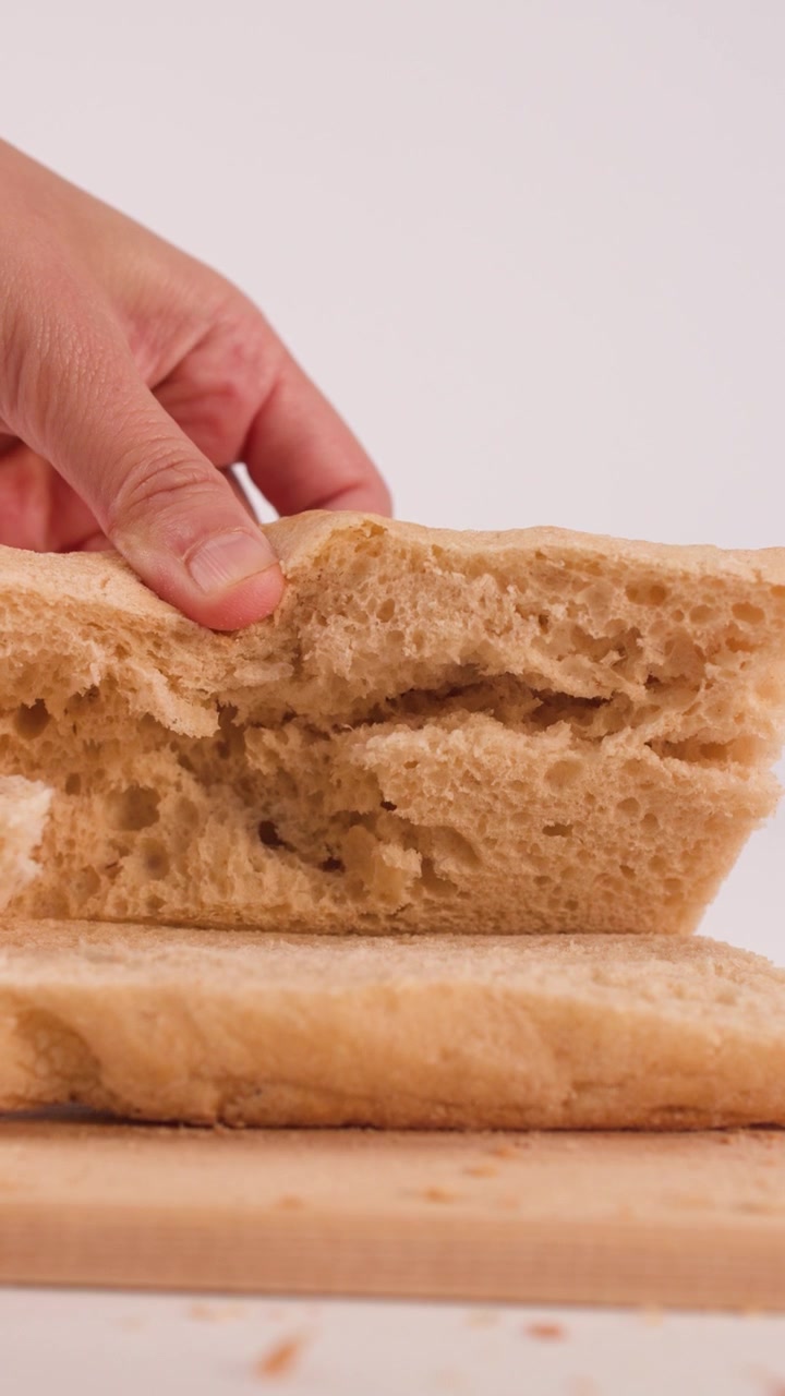 Close-up shot of hands lifting the top half of sliced sourdough bread on wooden board.