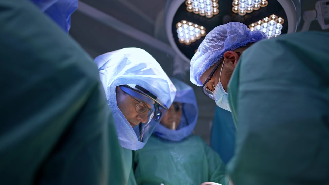Team of professional male surgeons in protective helmets work in the surgery room. Doctors use electric tools producing smoke going up. Trauma healing operation.