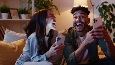 young couple or friends enjoying mobile content and laughing together on a sofa at home