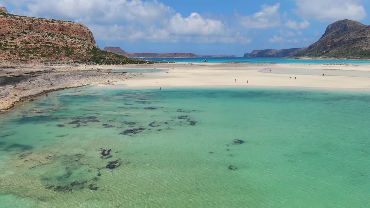 Balos Beach saltwater lagoon in Crete Greece with tourists enjoying the water and sun, Aerial flyover low altitude shot
