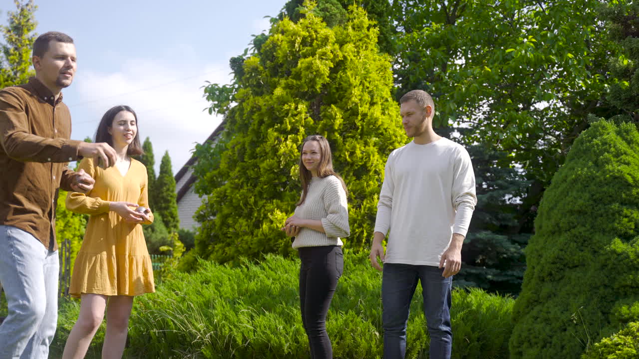 그의 친구들이 차례를 기다리는 동안 화창한 날 공원에서 페탕크 공을 던지는 백인 청년