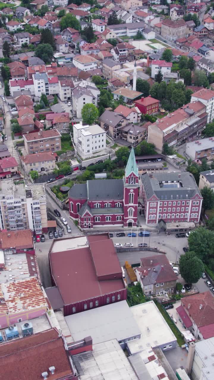 Vertical drone of red roofed Saint Anthony Church surrounded by Sarajevo cityscape, establishing overview