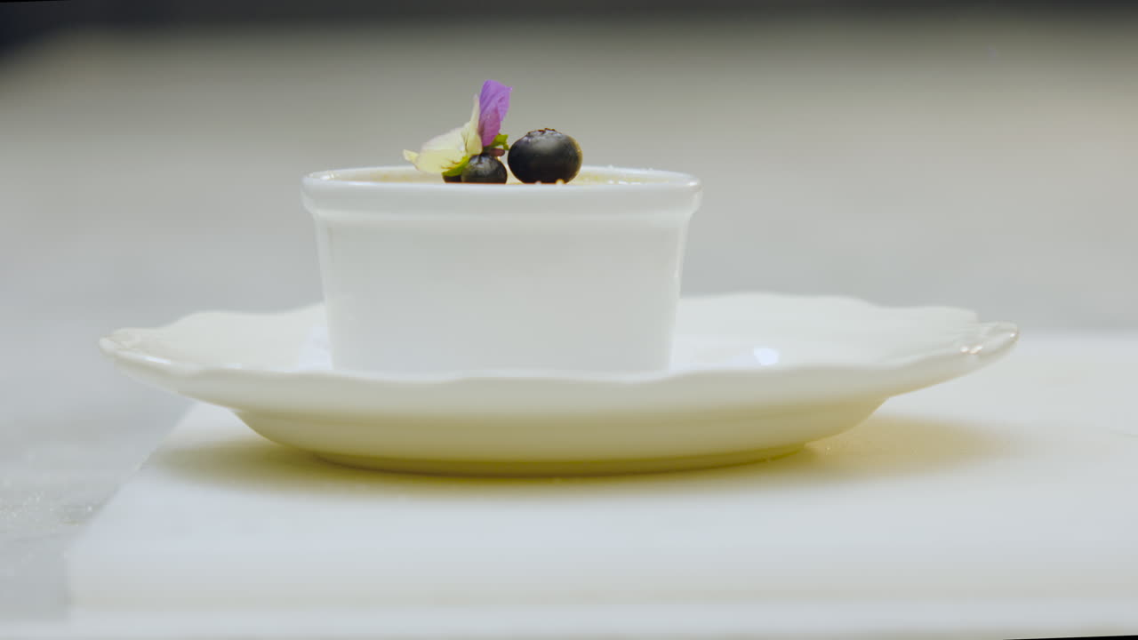 Close-up of a chef placing a creme brulee decorated with flowers and blueberries on a white plate