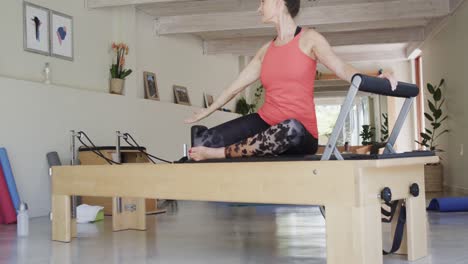 fit senior caucasian woman stretching on reformer in pilates studio, unaltered, in slow motion